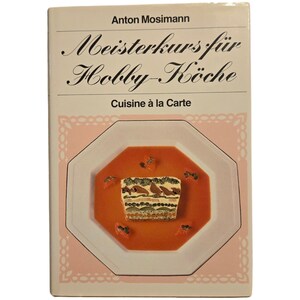 以下が含まれることがあります： 白い本の表紙に、黒い文字で「Meisterkurs für Hobby-Köche」というタイトルが書かれている。副題は「Cuisine à la Carte」で、より小さな黒い文字で書かれている。表紙には、赤い背景の白い八角形の皿があり、中央に重ねられた料理が置かれている。