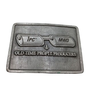 May include: Silver belt buckle with a graphic of two pipes connected with an arrow pointing down. The text "ipc®" is on one pipe and "MWD" is on the other. The text "OLD TIME PROFIT PRODUCERS" is below the pipes.