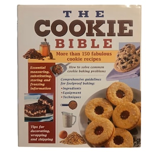 Peut inclure: La couverture du livre de cuisine "The Cookie Bible" présente une variété de biscuits, dont des pépites de chocolat, des biscuits fourrés à la confiture et des sablés. La couverture comprend également le texte "The Cookie Bible" et "Plus de 150 recettes de biscuits fabuleuses".