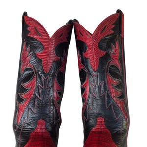 May include: A pair of cowboy boots in black and red. The boots feature a textured leather finish, with red panels and decorative stitching against a black background. The design is eye-catching.
