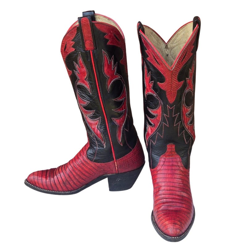 May include: A pair of cowboy boots in red and black. The boots feature a red, textured vamp and a black shaft with red decorative stitching. They have a pointed toe and a stacked heel.