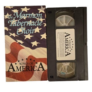 May include: A VHS tape of the Mormon Tabernacle Choir performing "Songs of America". The cover features an American flag with the choir's name and the title of the performance.