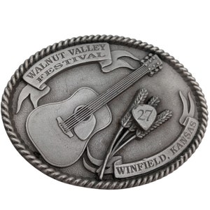 May include: A silver belt buckle featuring a guitar, wheat stalks, and the text "Walnut Valley Festival" and "Winfield, Kansas". The buckle also displays the number "27".