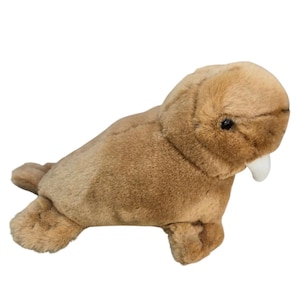 May include: A plush walrus toy made of soft, light brown fabric. The stuffed animal features a rounded head, small dark eyes, and a single white tusk protruding from the side of its mouth. It has flipper-like limbs and a textured, fuzzy surface.