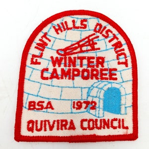 Może przedstawiać: Naszywka haftowana w kolorze czerwonym, białym i niebieskim z tekstem "Flint Hills District Winter Camporee BSA 1972 Quivira Council". Naszywka przedstawia stylizowany igloo z saniami w środku.