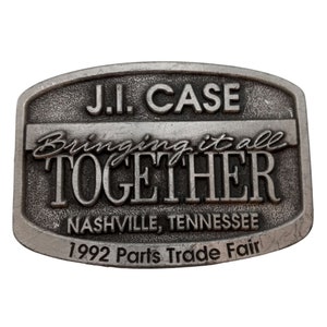 May include: A silver metal belt buckle with the text "J.I. Case Bringing it all TOGETHER Nashville, Tennessee 1992 Parts Trade Fair".
