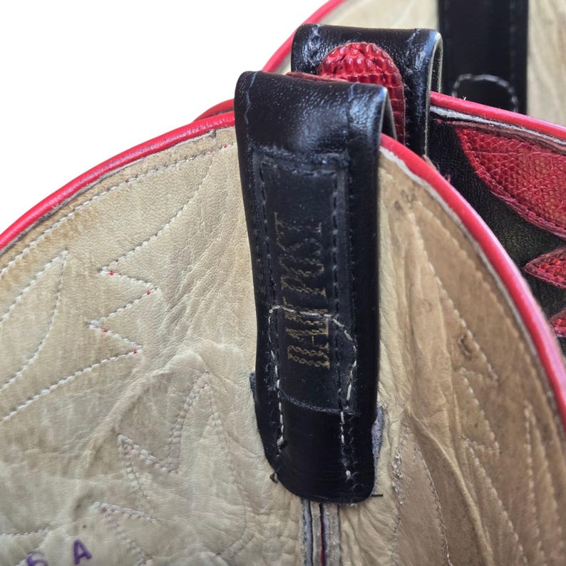 May include: Close-up of the interior of a red and black cowboy boot. The boot's interior is beige with a stitched pattern. A black leather pull tab is attached to the boot with the text "BOOT POST" visible.