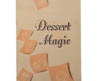 May include: A vintage cookbook cover, titled "Dessert Magic", featuring illustrations of desserts on peach-coloured squares. The cover is a light beige colour with the author's signature in the upper right corner. The title is in elegant script.