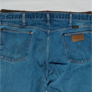 Puede incluir: Un par de pantalones vaqueros azules con un parche de cuero marr&oacute;n en el bolsillo trasero derecho que dice "Wrangler".