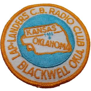Könnte beinhalten: Ein runder, orangefarbener gestickter Aufnäher mit dem Text "Blackwell, Oklahoma CB Radio Club" und einer weißen Umrandung des Bundesstaates Oklahoma mit den Worten "Kansas" und "Oklahoma" im Inneren.