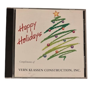 Puede incluir: Una caja de CD con un diseño festivo navideño. La portada presenta las palabras "Happy Holidays" en escritura roja, una ilustración de árbol de Navidad verde con adornos coloridos y una estrella dorada en la parte superior. También está presente el texto "Compliments of VERN KLASSEN CONSTRUCTION, INC.".