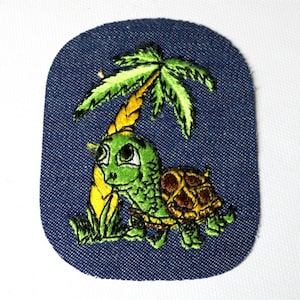 May include: Embroidered patch featuring a cartoon turtle under a palm tree. The turtle is green with a brown shell, and the palm tree has green fronds. The patch is on a blue denim background.