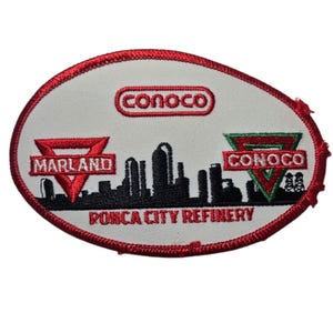 May include: Oval-shaped patch with a white background and a red border. The patch features the Conoco logo in red, the Marland logo in red, and the Conoco logo in green. A black silhouette of a city skyline is in the center, with the text "PONCA CITY REFINERY".
