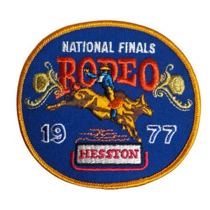 May include: A blue and gold embroidered patch with the text "National Finals Rodeo 1977" and a cowboy riding a bucking bull. The text "Hesston" is in a red rectangle.