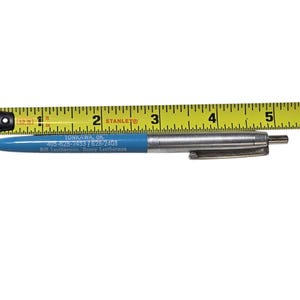 Puede incluir: Un bolígrafo azul y plateado con un clip, junto a una cinta métrica amarilla. El bolígrafo tiene el texto "TONKAWA, OK" y un número de teléfono. El bolígrafo mide unos 13 cm de largo.