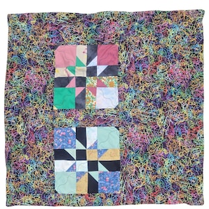 Puede incluir: Un edredón hecho a mano con un fondo negro cubierto de líneas onduladas de colores. Dos diseños de patchwork cuadrados están centrados en el edredón, con varias telas en rosa, azul, verde y negro.