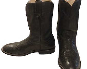 Könnte beinhalten: Ein Paar schwarze Cowboy-Stiefel. Die Stiefel sind aus strukturiertem Leder gefertigt und haben ein klassisches Western-Design. Die Stiefel haben eine spitze Zehenpartie und einen gestapelten Absatz. Die Nähte sind um die Sohle sichtbar.