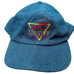 Può includere: Un berretto da baseball in denim blu con un logo ricamato in giallo, rosso e bianco che dice "IronKids USA Triathlon".