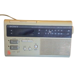 May include: A beige Sony Dream Machine dual alarm FM/AM digital clock radio. The radio has a digital display, buttons for radio, buzzer, sleep, and alarm reset. The radio has a built-in antenna and a speaker.