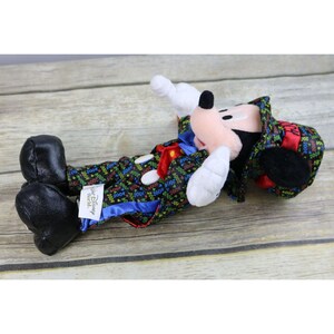 May include: A plush Mickey Mouse wearing a black tuxedo with a red bow tie and a top hat. The tuxedo is covered in colorful 2000s printed text. The plush is labeled "Walt Disney World".