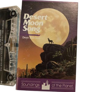 May include: A cassette tape with a cover featuring the text "Desert Moon Song" and the artist's name, Dean Evenson. The cover art depicts a full moon, a howling wolf, and desert landscape. The cassette is clear plastic.
