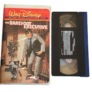 May include: A VHS tape of the Disney film "The Barefoot Executive" from The Kurt Russell Collection. The cover features a man in a suit and a chimpanzee. The tape is black with a blue spine.