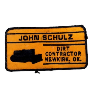 Puede incluir: Un parche bordado amarillo y negro con el texto "JOHN SCHULZ DIRT CONTRACTOR NEWKIRK, OK."