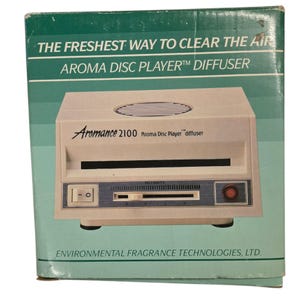 Puede incluir: Un difusor Aroma Disc Player 2100 blanco con una luz roja y un dial de intensidad. La caja dice "The Freshest Way to Clear the Air Aroma Disc Player Diffuser".
