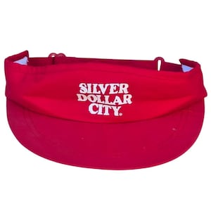 May include: A red visor with the words "SILVER DOLLAR CITY" in white block letters. The visor has a curved brim and an adjustable strap. The visor is made of a lightweight material.