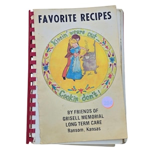 Peut inclure: Un livre de cuisine vintage à reliure spirale intitulé Favorite Recipes par Friends of Grisell Memorial Long Term Care à Ransom, Kansas. La couverture présente une illustration circulaire jaune de deux personnes cuisinant avec le texte Kissin' wears out... Cookin' don't!