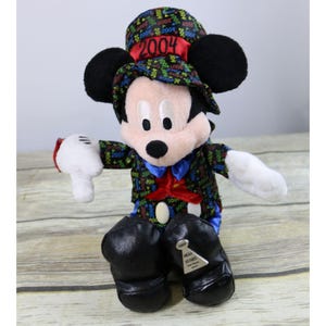 May include: A plush Mickey Mouse wearing a black and multi-colored tuxedo with a top hat that says "2004" on it. The plush is sitting down with its arms outstretched. The plush has a tag that says "Happy New Year's 2004".