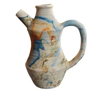 May include: A handmade ceramic pitcher with a spout and handle. The pitcher features a marbled design with blue, orange, and white hues. The pitcher is a unique piece of art pottery.