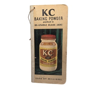 May include: A vintage cookbook cover featuring a yellow and red illustration of a glass jar of KC Double Action Baking Powder. The text on the cover reads "KC Baking Powder packed in re-usable glass jars. Used by millions."