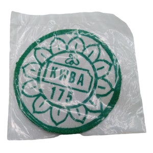 May include: A green and white embroidered patch with the text "KWBA 17.5" inside a circle with a flower design.