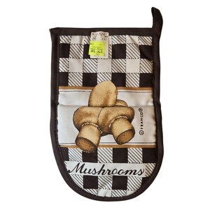 Puede incluir: Manopla de horno marrón y blanca con diseño de setas. La manopla presenta un patrón de cuadros marrones y blancos con una imagen central de tres setas. La palabra "Mushrooms" está impresa en la parte inferior.
