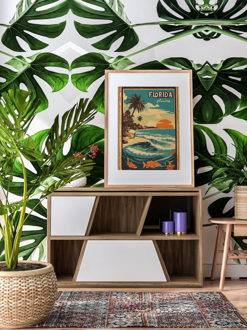 May include: A framed vintage travel poster with the text "Florida" and a depiction of a beach scene with palm trees, waves, and a surfer. The poster is displayed on a wooden shelf with a white front panel and purple candles.