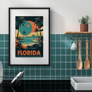 Peut inclure: Une affiche encadr&eacute;e avec un design r&eacute;tro repr&eacute;sentant une sc&egrave;ne de plage avec des palmiers et un grand orbe orange et bleu dans le ciel. L'affiche indique "FLORIDA" en lettres orange et grasses.