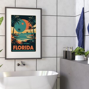 Peut inclure: Une affiche encadr&eacute;e avec un design r&eacute;tro repr&eacute;sentant une sc&egrave;ne de plage avec des palmiers et un grand cercle bleu et orange. Le texte "FLORIDA" est imprim&eacute; en orange en bas de l'affiche.