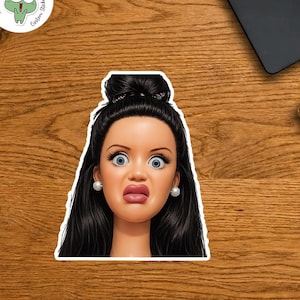 Pode incluir: Um adesivo com um rosto de boneca com uma expressão surpresa, olhos azuis grandes e cabelo escuro. O adesivo tem uma borda branca e o texto "THUY LINH Custom Stickers". O adesivo está em uma superfície de madeira.