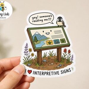 May include: A die-cut sticker featuring an outdoor interpretive sign with a smiling face, a small bird perched on top, and a speech bubble that says, "yay! someone's reading me!!!". The text "I [heart symbol] INTERPRETIVE SIGNS" is below.