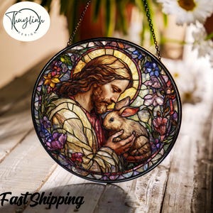 Puede incluir: Vidriera redonda que representa a Jesús sosteniendo un conejo, rodeado de flores coloridas. La obra de arte tiene un marco de metal negro y está suspendida por una cadena. La imagen incluye el texto "Fast Shipping" en la parte inferior.