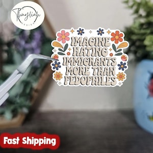 Op de afbeelding: Een sticker met de tekst "IMAGINE HATING IMMIGRANTS MORE THAN PEDOPHILES" in een retro lettertype, versierd met bloemen- en stermotieven. De sticker wordt vastgehouden door een pincet.