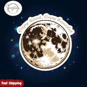 Pode incluir: Um autocolante com uma ilustração detalhada da lua em tons de castanho e bege, com o texto "Copy heart, Copy bracelet" numa faixa curva. O fundo é azul escuro com estrelas.