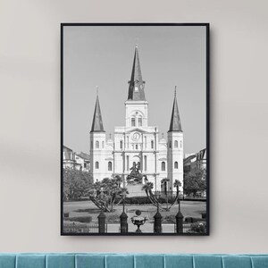 Puede incluir: Fotografía en blanco y negro de la Catedral de San Luis en Nueva Orleans, Luisiana. La catedral es un edificio grande y blanco con tres torres y un reloj en la fachada.