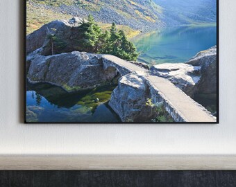 Puede incluir: Una fotografía panorámica de un puente de piedra sobre un lago de montaña. El puente está hecho de piedra toscamente labrada y conduce a una pequeña isla en medio del lago. El lago está rodeado de exuberantes montañas verdes y el agua es de un color azul profundo.
