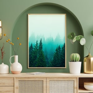 May include: A wooden console table with two drawers and two cabinet doors with a woven rattan front. The table is decorated with a framed print of a foggy forest, a gold vase with a leafy plant, a white vase with a cactus, and two white vases with yellow flowers.