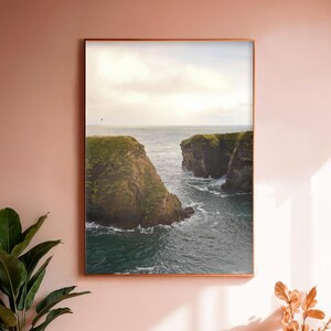 May include: A photograph of a rocky coastline with a deep blue ocean. The cliffs are covered in green grass and the water is crashing against the rocks.
