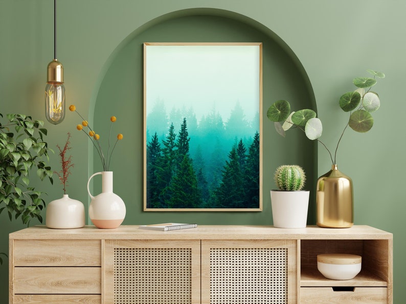 May include: A wooden console table with two drawers and two cabinet doors with a woven rattan front. The table is decorated with a framed print of a foggy forest, a gold vase with a leafy plant, a white vase with a cactus, and two white vases with yellow flowers.