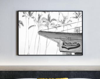 Puede incluir: Impresión en blanco y negro enmarcada con un letrero que dice "Chillville" en una fuente de escritura. El letrero está debajo de un techo, con palmeras al fondo. La impresión se muestra encima de una cama.