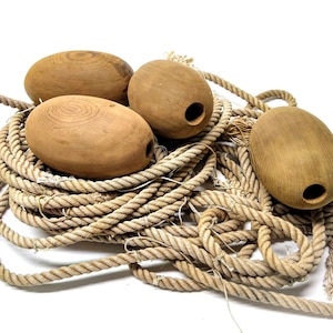 Peut inclure: Quatre bouées en bois de couleur naturelle reposent sur une grosse corde enroulée. Les bouées sont de forme ovale avec un trou percé dans chacune d'elles. La corde est de couleur beige clair, et le fond est blanc.